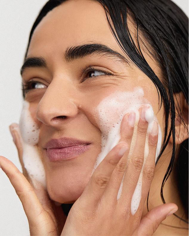 Woman with wet hair massaging a white foaming Inskin Co cleanser over her cheeks and nose.