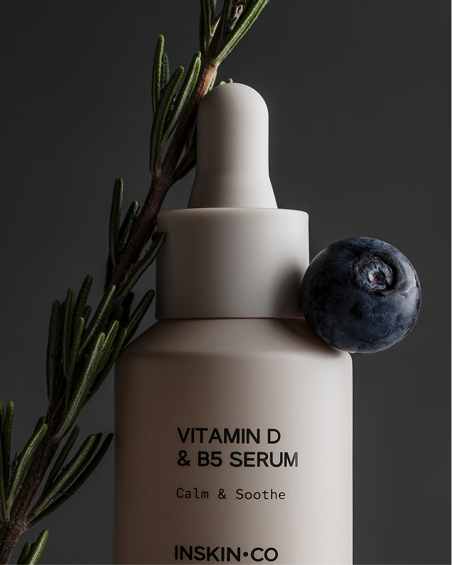 Inskin Co Vitamin D & B5 Calm & Soothe serum in a matte dropper bottle beside a rosemary sprig and a blueberry.